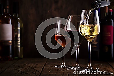 Wine tasting. White wine pouring into glass on background with selection of red, white and rose wines in glasses and bottles Stock Photo