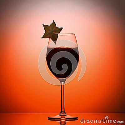 Wineglass liquid cocktail decorated with carambola in studio orange background Stock Photo