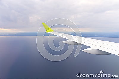 Wing of an airborne airplane ocean below. the plane flies over the water. clear blue sky Stock Photo