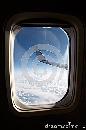 Wing of an airplane above the blue clouds in porthole Stock Photo