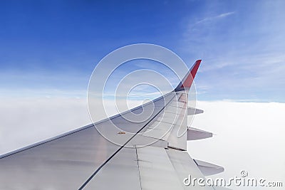 Wing of commercial airplane view from right the window of the plane flying above the clouds on blue sky Stock Photo
