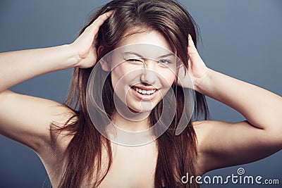 Wink, face and beauty portrait of a woman in studio with a smile, makeup and hands in hair. Headshot of a happy female Stock Photo