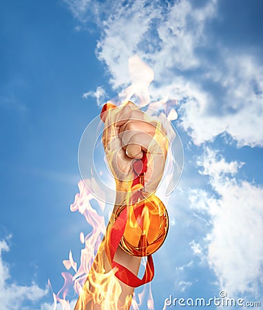 Winner raising hand with gold medal from fire flames up to sky, closeup Stock Photo