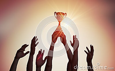 Winning team is holding trophy in hands. Silhouettes of many hands in sunset Stock Photo