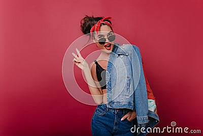 Winsome trendy lady in stylish sunglasses having fun during indoor photoshoot. Lovable girl sitting in studio and posing Stock Photo