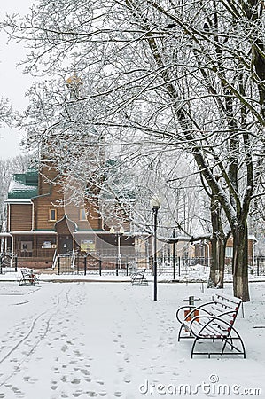 Winter alley, benches and footprints, wooden church under tall Stock Photo