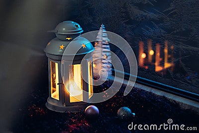 Winter Christmas Eve. Frosted window with Christmas decoration. Lantern with a lit candle near the window with frosty patterns on Stock Photo