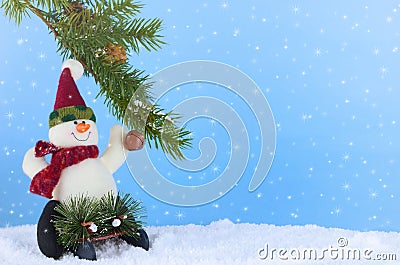 Winter Christmas scene of cute plush snowman playing on sled underneath a pine branch in artificial snow. Stock Photo