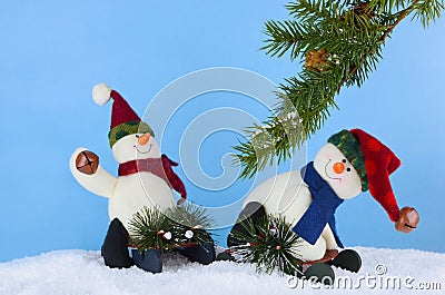 Winter Christmas scene of cute plush snowmen playing on sleds underneath a pine branch in artificial snow. Stock Photo