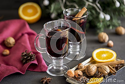 Mulled wine in glasses at black background. Fir wreath, tray with orange, cinnamon, nuts, cone and spices near Stock Photo