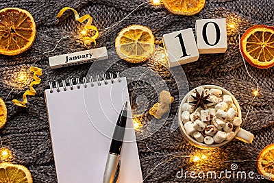 Winter composition. Wooden calendar January 10th Cup of cocoa with marshmallow, empty open notepad with pen, dried oranges, light Stock Photo