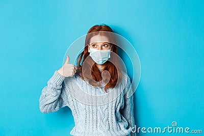 Winter, covid-19 and social distancing concept. Satisfied young redhead woman in face mask showing alright, thumb up Stock Photo