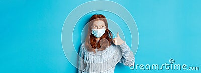 Winter, covid-19 and social distancing concept. Satisfied young redhead woman in face mask showing alright, thumb up Stock Photo