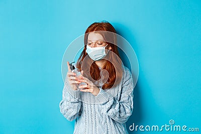 Winter, covid-19 and social distancing concept. Young redhead woman in face mask clean hands with antiseptic Stock Photo