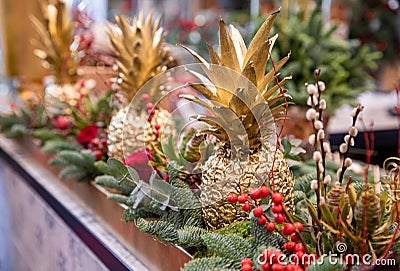 Winter decor. Beautiful arrangement of golden colored pineapples, red roses, natural sprigs of blue spruce and Christmas berry Stock Photo