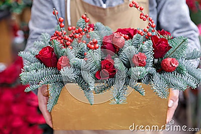 Winter decor. Beautiful flower arrangement of red roses, natural sprigs of blue spruce and Christmas berry holly or ilex twigs, Stock Photo