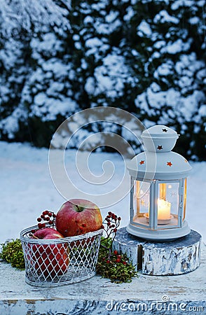Winter evening in the garden. Iron lantern and basket of apples Stock Photo
