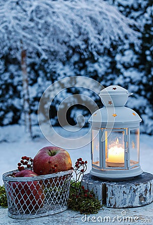 Winter evening in the garden. Iron lantern and basket of apples Stock Photo