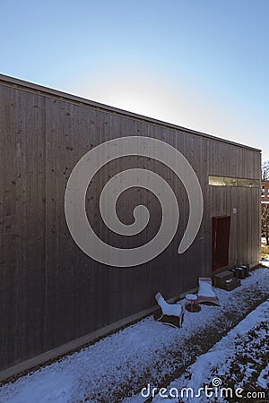 Winter exterior of modern small wooden house. At the entrance two garden chairs with snow Stock Photo