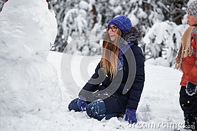 Winter fun. girl in a knitted hat sculpts a snowman. Stock Photo