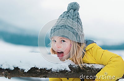 Winter girl eating snow outdoor. Funny christmas kids holiday. Kids cold and flu concept. Kid lick snow with tongue Stock Photo
