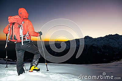 Winter hiking: man stands on a snowy ridge looking at the sunset Stock Photo