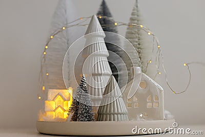 Winter hygge, cozy christmas magical scene, miniature snowy village with lights. Stylish little Christmas trees and house on white Stock Photo