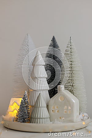 Winter hygge, cozy christmas magical scene, miniature snowy village with lights. Stylish little Christmas trees and house on white Stock Photo