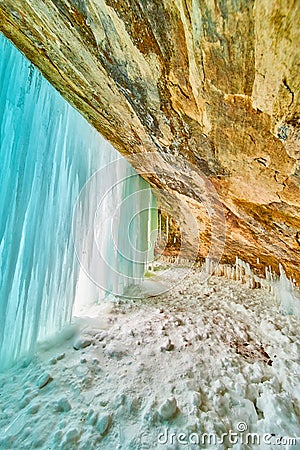 Winter ice cavern entrance blocked by frozen waterfall sheet of blue ice and icicles Stock Photo