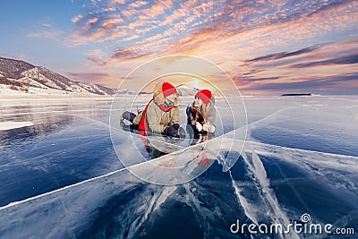 Winter lake Baikal Russia, two tourist women friends in red cap are skating on ice frozen sunset Stock Photo