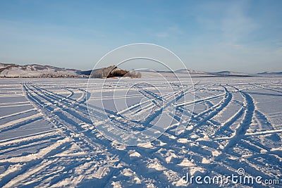 Car tracks go across the frozen Great Lake to the island against the backdrop of the village of Parnaya, Krasnoyarsk Territory. Stock Photo