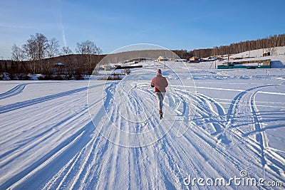 Girl runs along a winter road on a frozen lake towards a village on a hill, on a winter sunny day Stock Photo