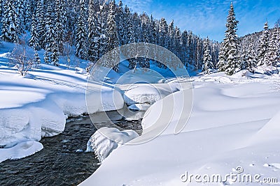 Mountain stream going through the snow into the depths of the forest Stock Photo