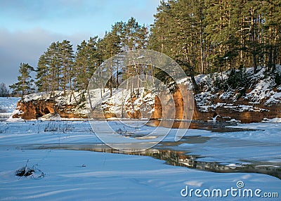 Winter landscape with red sandstone cliffs on the bank of the river Salaca, the sun shines on the trees and the river bank, the Stock Photo