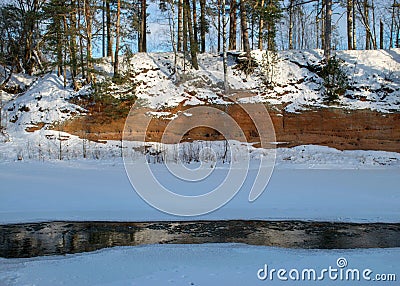 Winter landscape with red sandstone cliffs on the bank of the river Salaca, the sun shines on the trees and the river bank, the Stock Photo