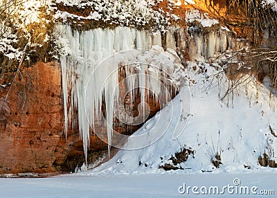 Winter landscape with red sandstone cliffs and icefall on the bank of the river Salaca, the sun shines on the trees and the bank Stock Photo