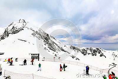 Winter landscape. Snow covered high mountain peaks under cloudy panoramic skies in Europe. Downhill skiers and snowboarders. Stock Photo