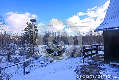 Winter landscape with the stork nest on wooden pole, rural house building details and snow covered field Stock Photo