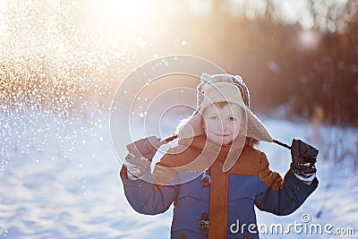 Winter little child playing throws up snow outdoors during snowfall. Active outoors leisure with children in winter on cold snowy Stock Photo