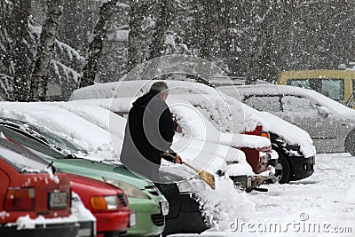 Winter. A man with a broom cleans car from snow on the street after big snowstorm in the city, all cars under snow, icy roads, sno Editorial Stock Photo