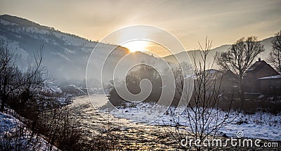 Winter mist landscape with mountains, river and houses Stock Photo