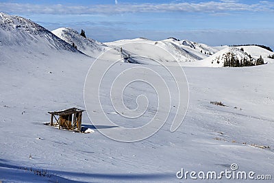 Winter mountain background with small wooden alpine cottage, on a snow field Stock Photo