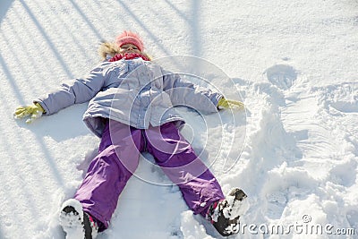 Winter portrait of cheerful child girl having fun in the snow, lying on the snow in the form of angel, top view Stock Photo