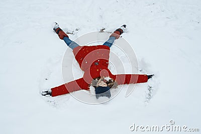 Winter portrait of cheerful girl having fun in the snow, lying on the snow in the form of angel, top view Stock Photo