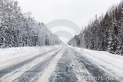 Winter road with ice on the asphalt, trees under snow during the winter frost Stock Photo