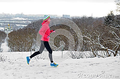 Winter running in park: happy active woman runner jogging in snow with Kyiv city skyline view, outdoor sport and fitness Stock Photo