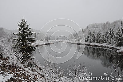 Winter Scenery Season Photo and Image. Horizontal Photo. Displaying its white blanket on trees, river and with a grey sky with a Stock Photo