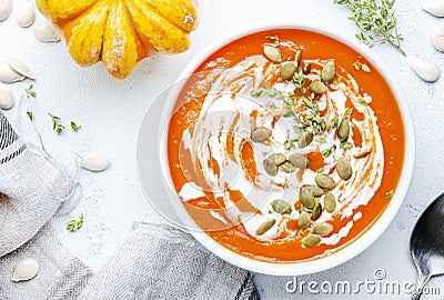 Winter slow food. Pumpkin carrot soup with cream, seeds and thyme.. Healthy diet food. White soup bowl on gray table background. Stock Photo