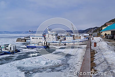Winter snowy port with white ships on the icy shore of baikal, blue mountains in background Editorial Stock Photo