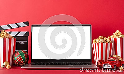 Winter staycation: side view of laptop, popcorn, baubles, movie clapper red wall backdrop for advertising Stock Photo